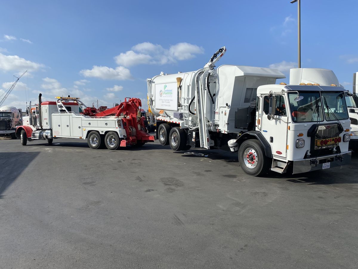 Hadley Peterbilt heavy-duty towing a Peterbilt refuse truck under clear skies