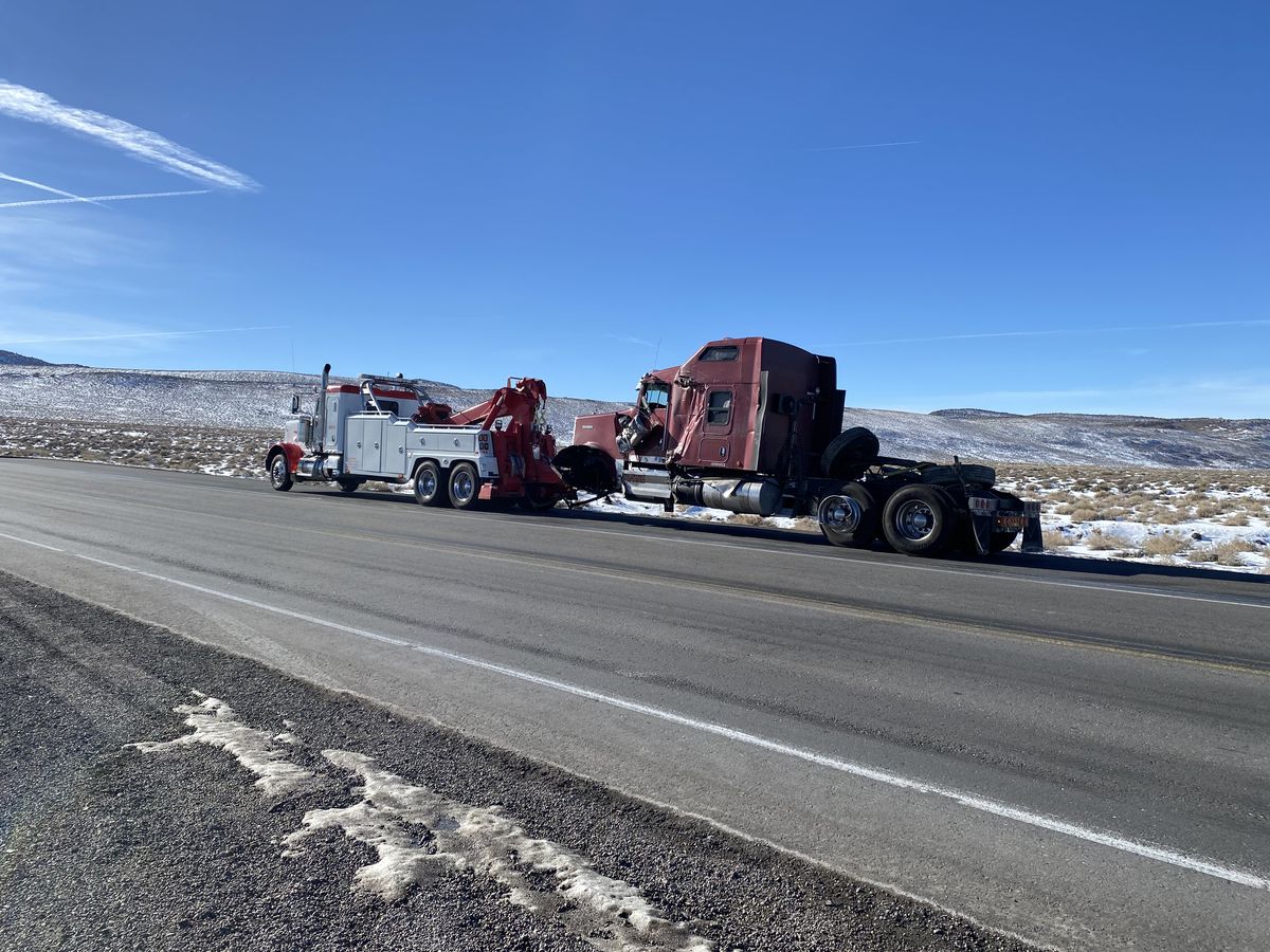 Hadley heavy wrecker towing a red Peterbilt tractor along a snowy desert highway